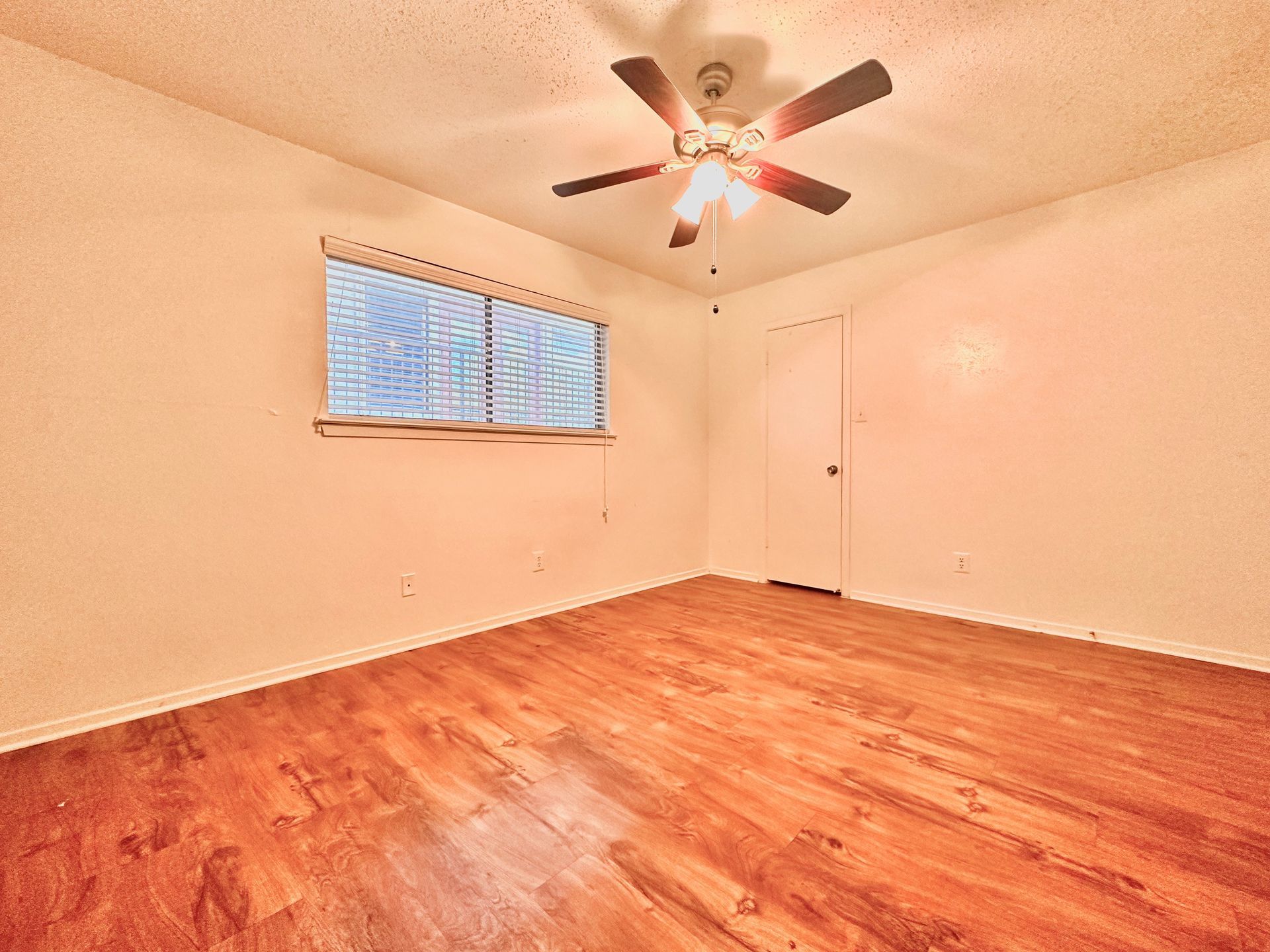 An empty bedroom with hardwood floors and a ceiling fan.