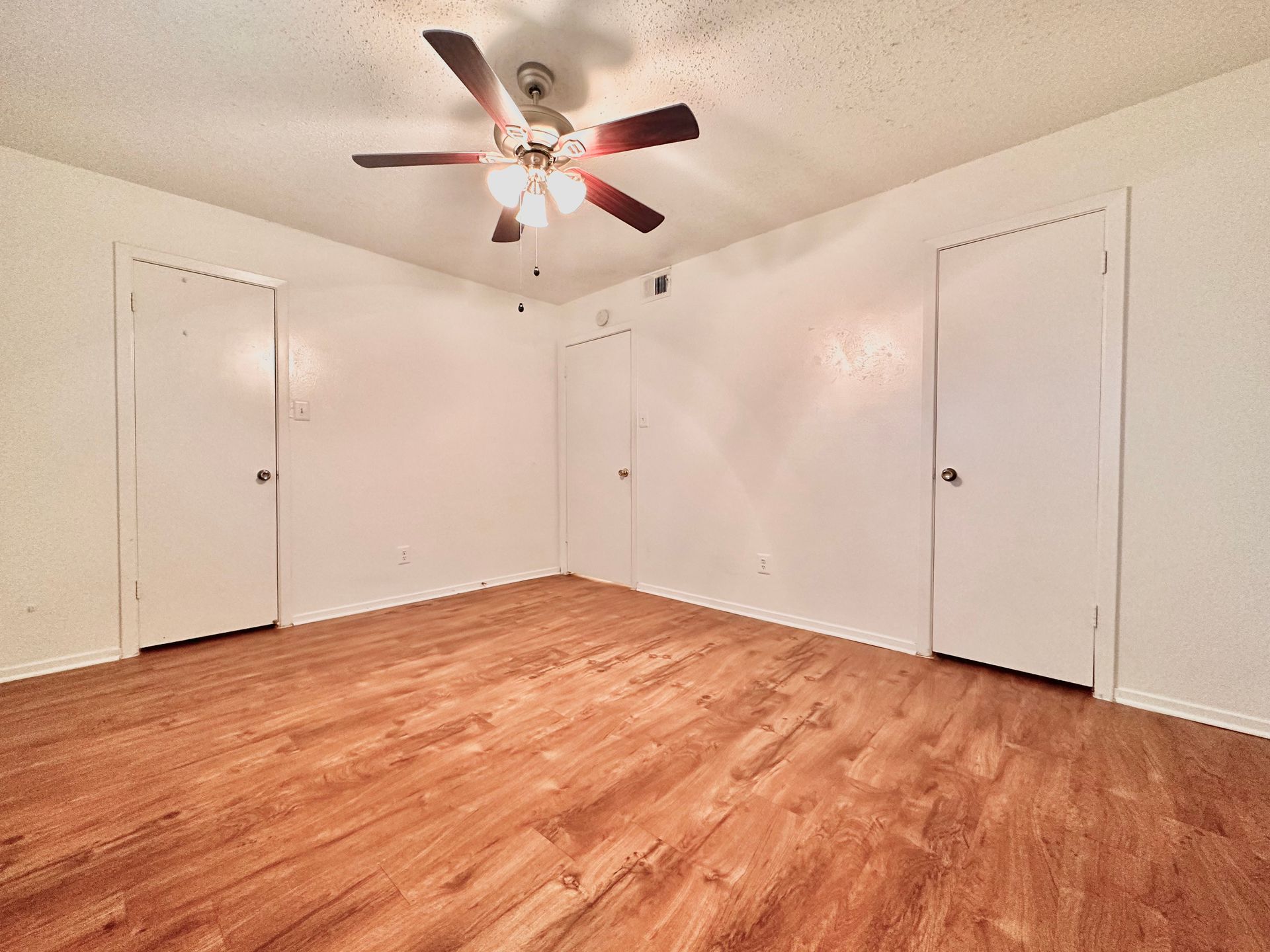 An empty room with hardwood floors and a ceiling fan.