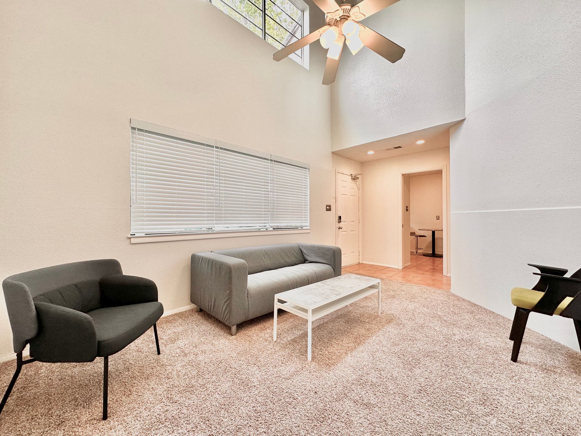 A living room with a couch , chair , coffee table and ceiling fan.