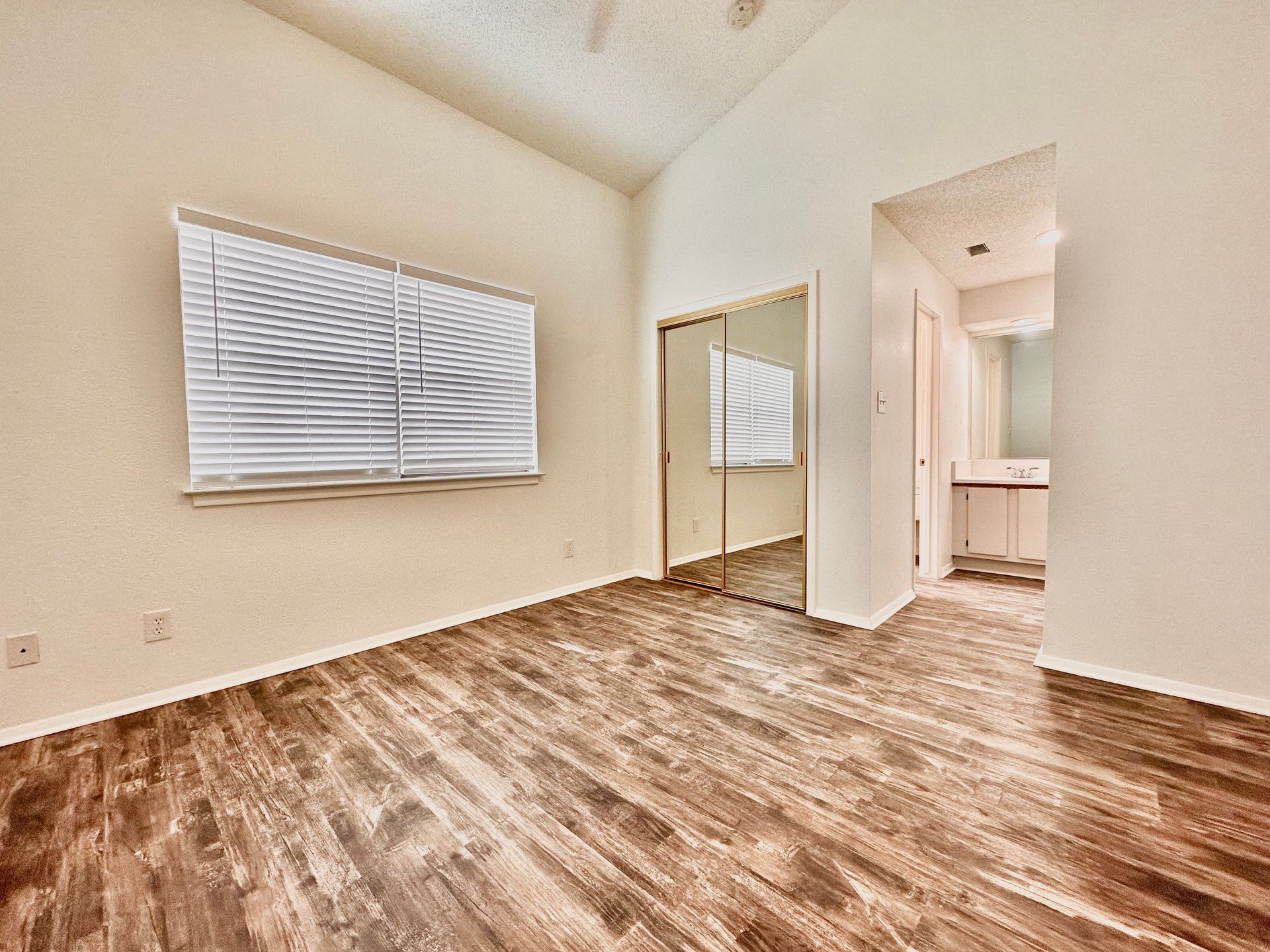 An empty bedroom with hardwood floors and a large mirror.
