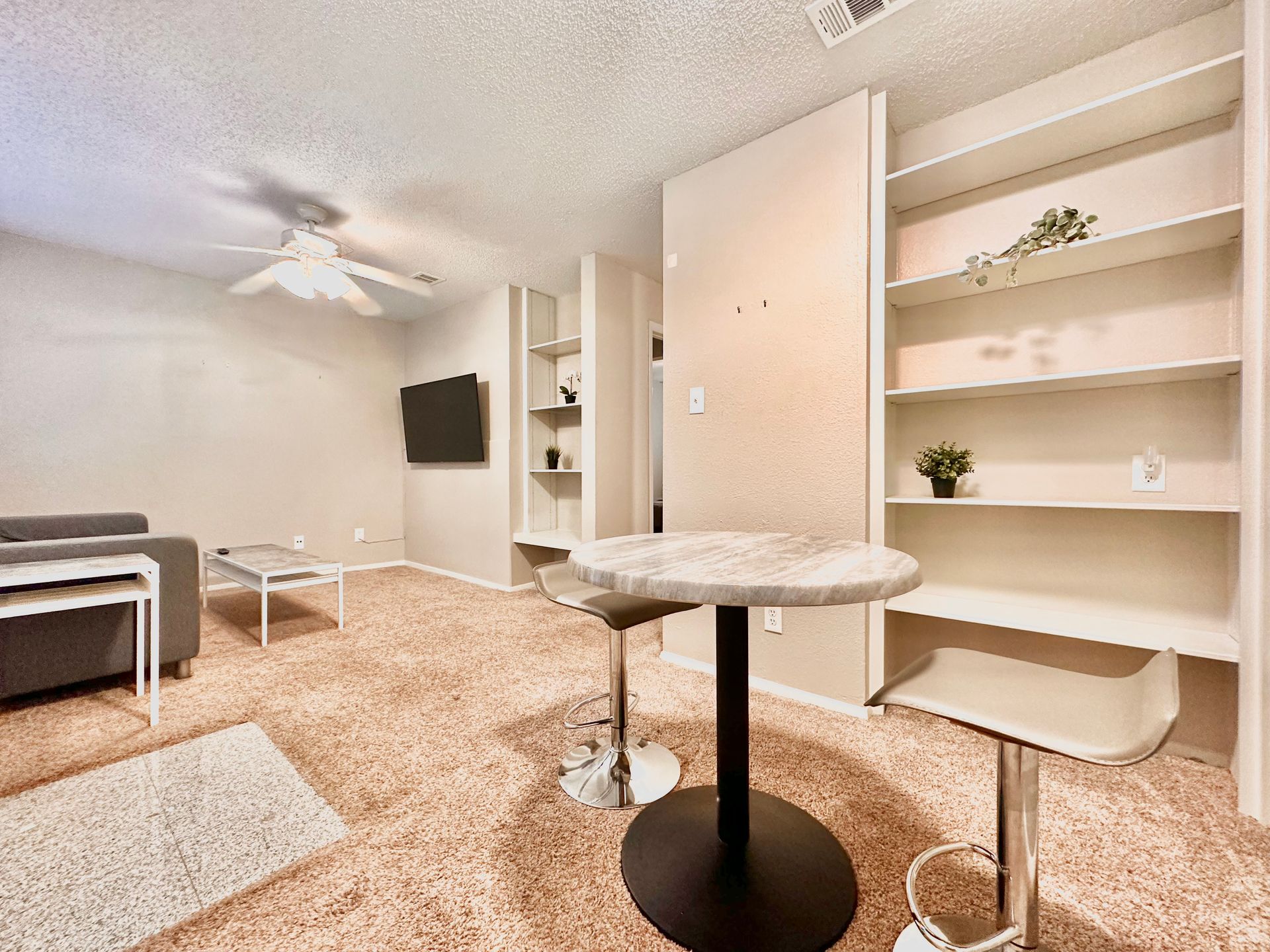 A living room with a table and stools and a ceiling fan.