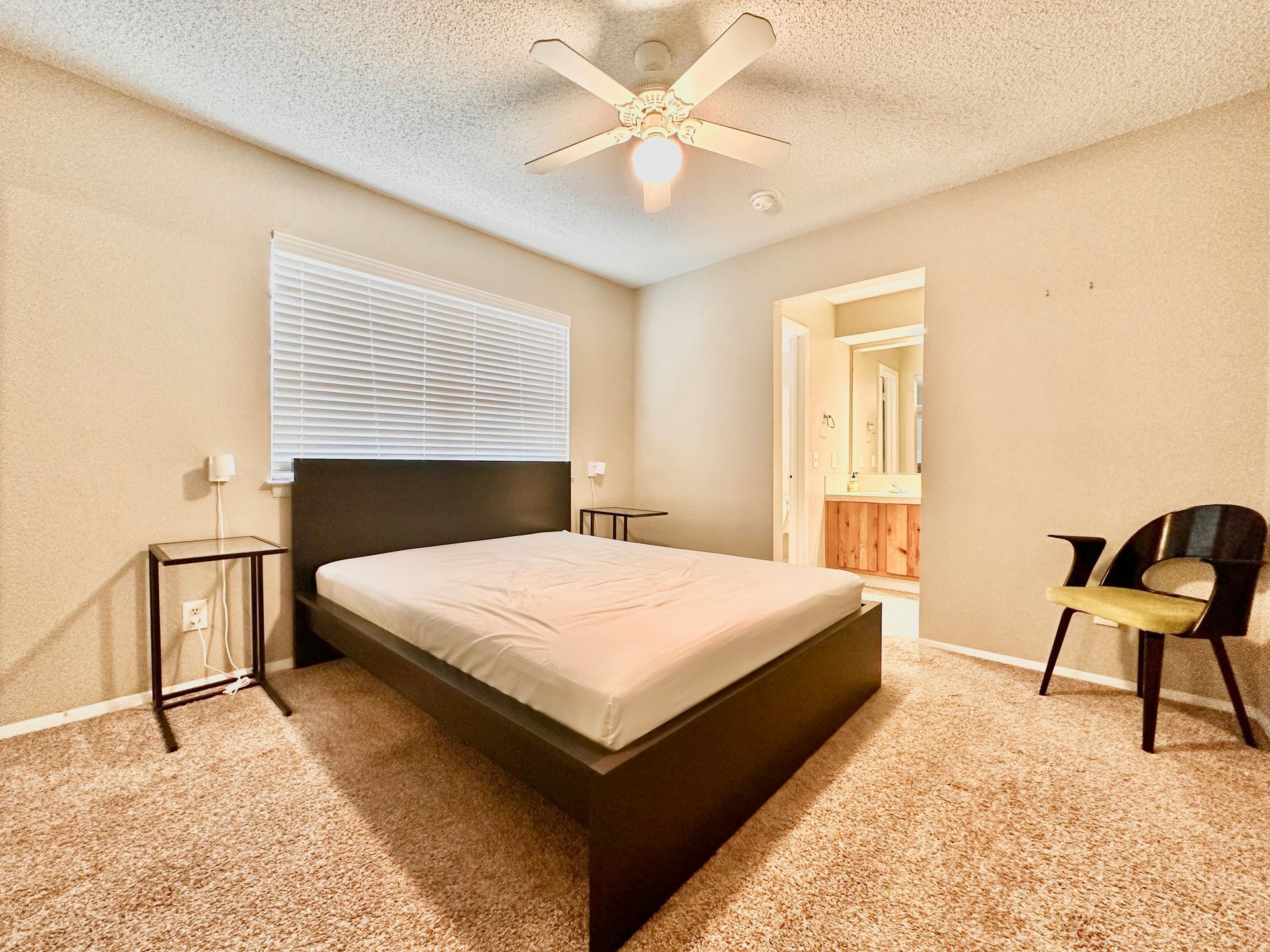 A bedroom with a bed , chair , nightstand and ceiling fan.