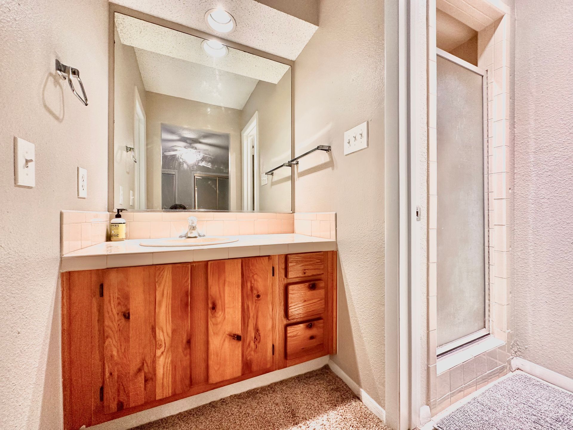 A bathroom with a sink , mirror and walk in shower.