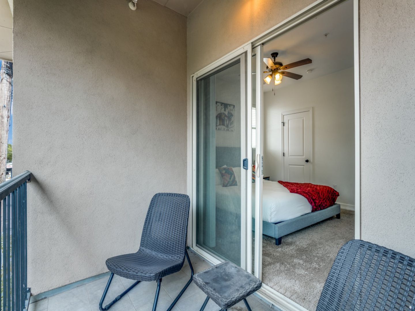 A balcony with chairs and a table with a sliding glass door leading to a bedroom.