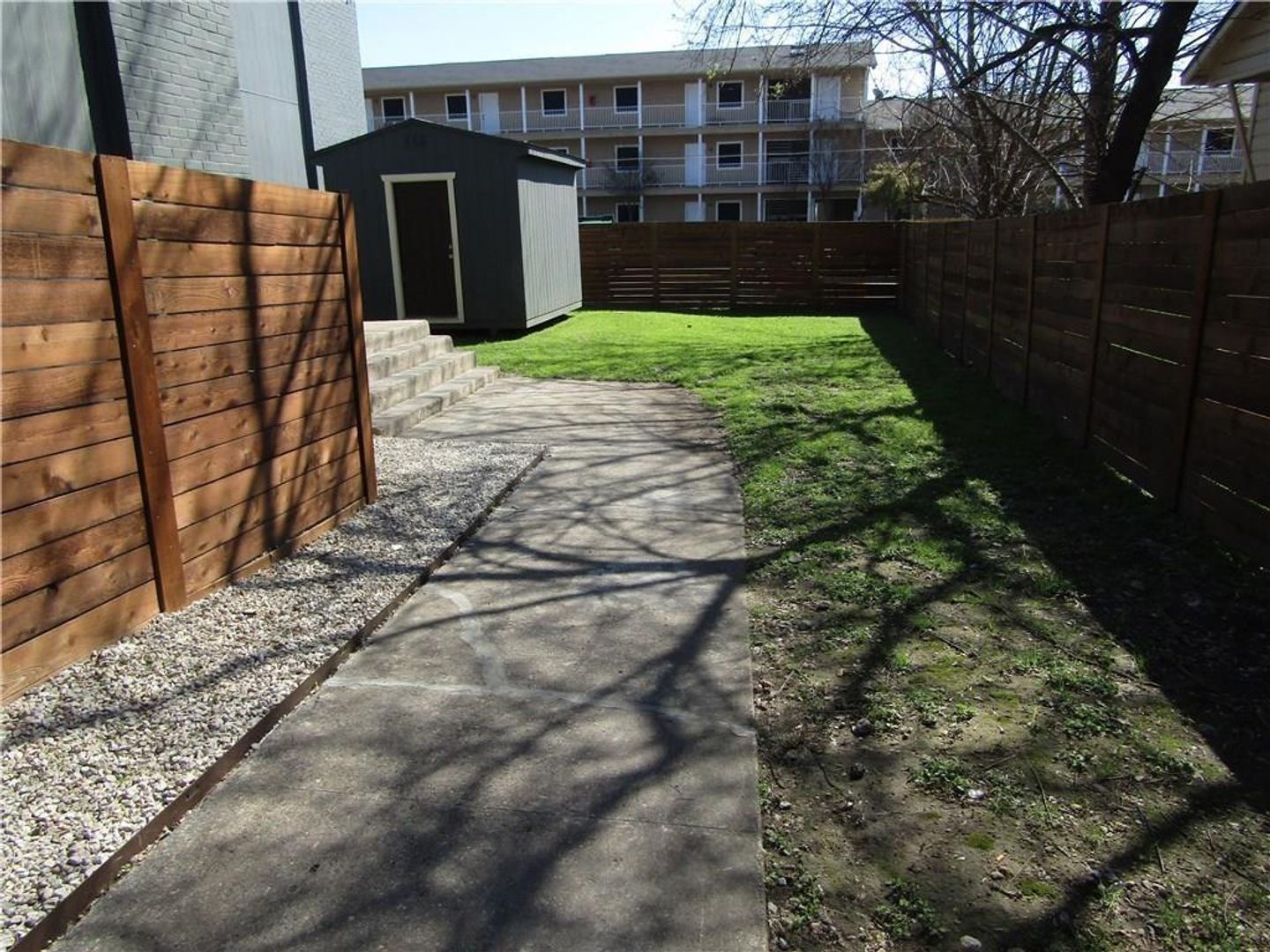 A fenced in backyard with a shed and a walkway
