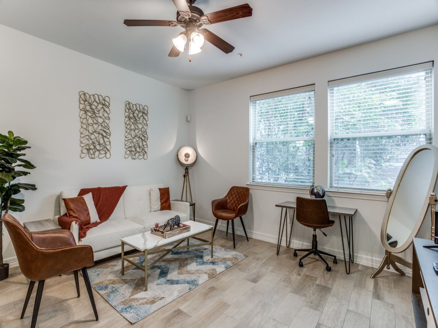 A living room with a couch , chairs , a desk and a ceiling fan.