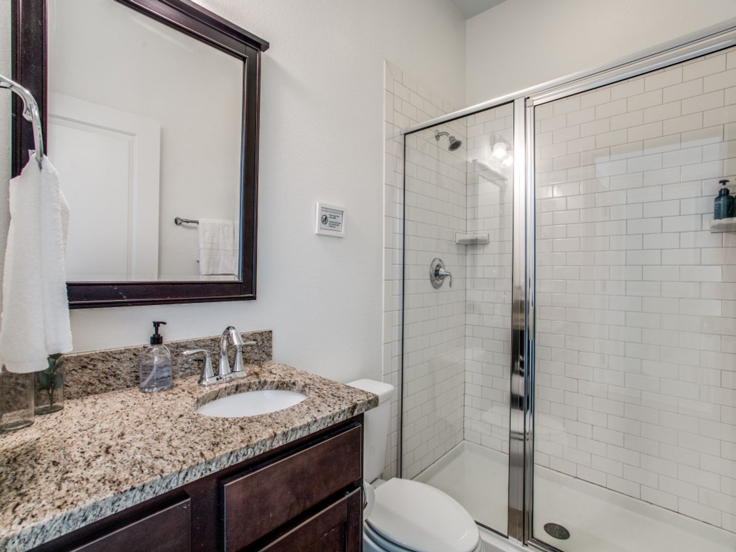 A bathroom with a toilet , sink , mirror and walk in shower.