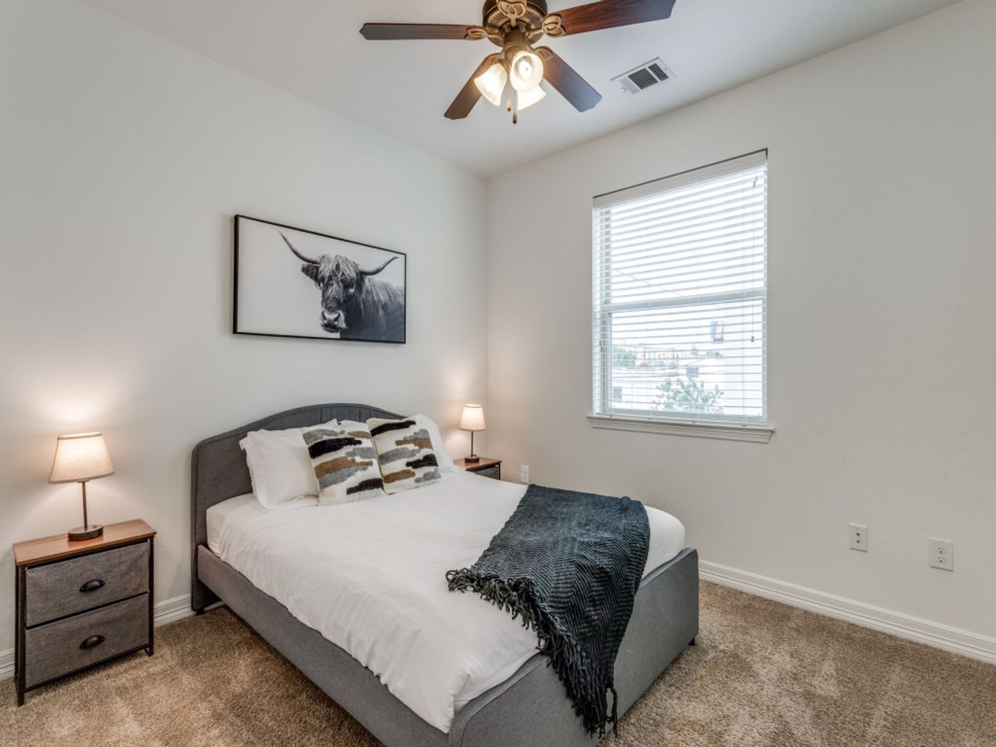 A bedroom with a bed , nightstand , lamp and ceiling fan.