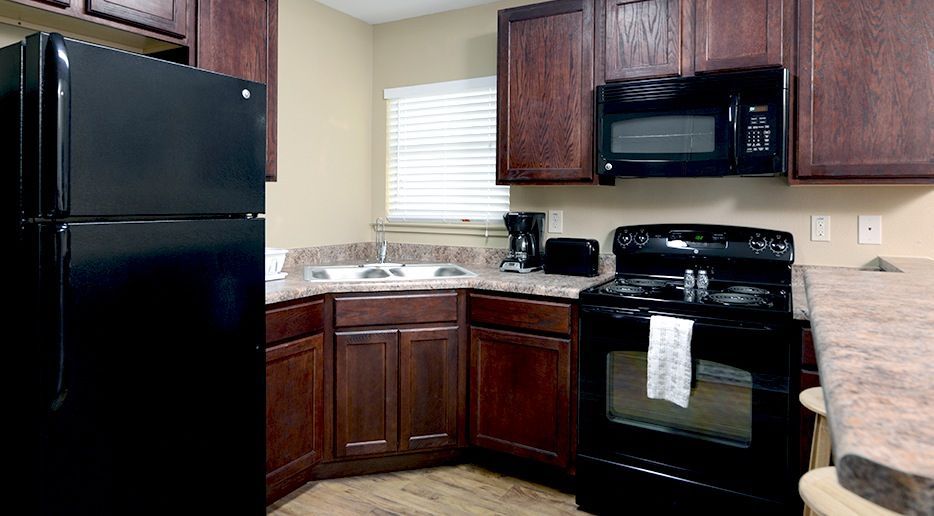 A kitchen with a black refrigerator , stove , microwave and sink.