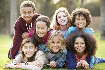 A group of six children smiling together on grass outdoors.