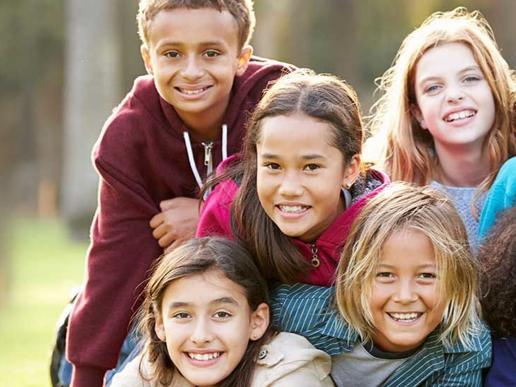 Seven smiling children posing outdoors in a piggyback-style group photo