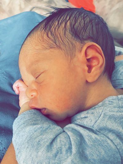 Sleeping newborn in a gray outfit, resting on a blue blanket with a pink pacifier nearby