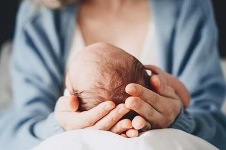 Adult holding a newborn baby’s head in both hands, close-up in a soft blue setting