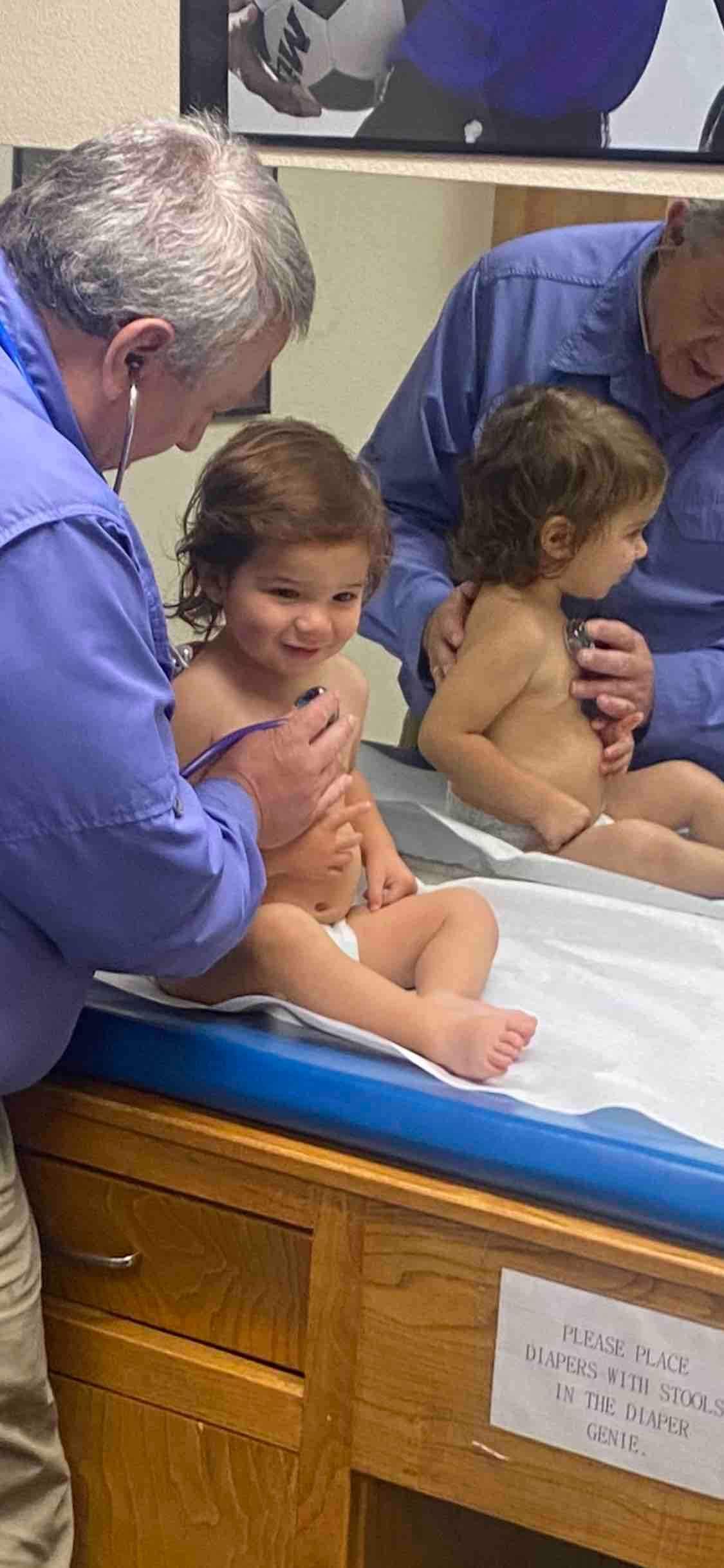 Adult helping two children sit in a blue-tiled pool or bath area, with water around them.