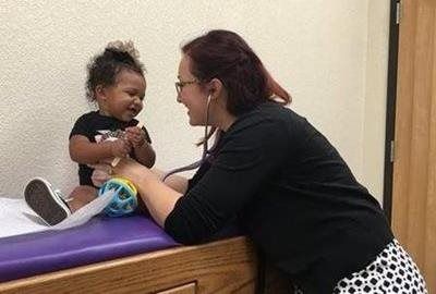 Woman smiling at a toddler on a padded exam table in a clinic room