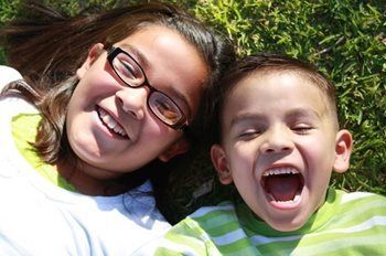 Two smiling children lying on grass, one wearing glasses and both in bright green shirts
