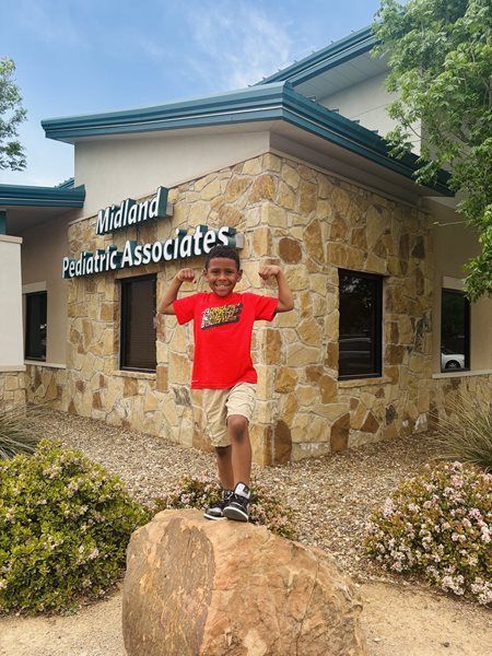 Person in a red shirt posing on a rock outside Hallard Pediatric Associates.