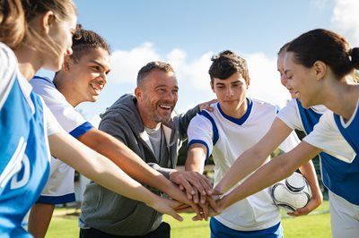 Soccer team and coach stacking hands in a huddle on a sunny field