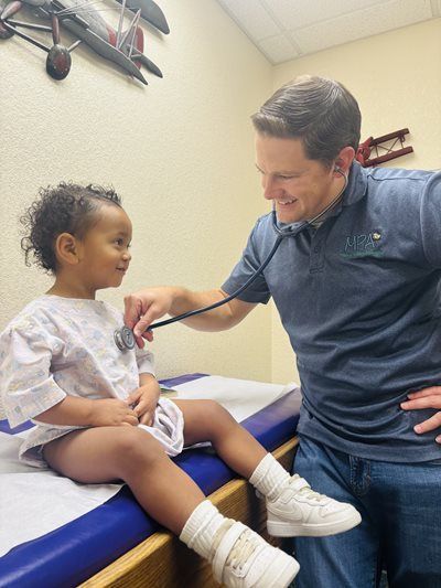 Doctor examines a smiling child on an exam table in a clinic room.