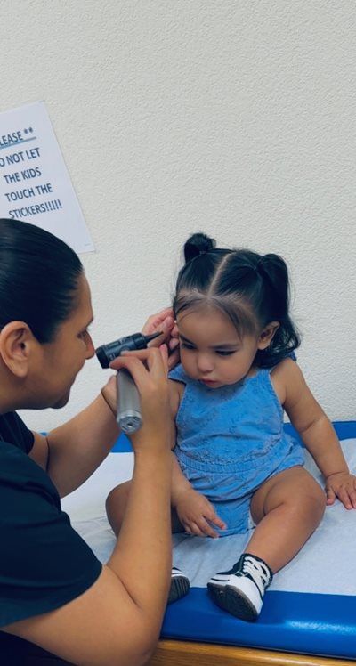 Clinician using an otoscope to examine a child’s ear in a medical exam room