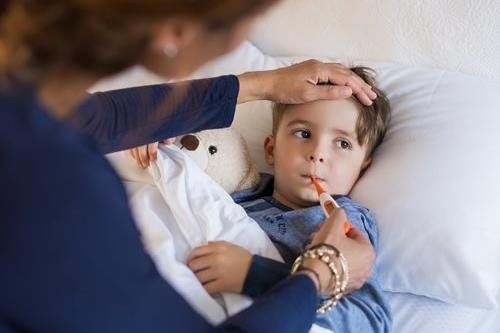 Adult checking a child’s temperature in bed with a thermometer