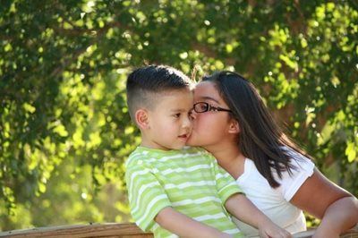 Woman kissing a child on the cheek outdoors in a sunny green park