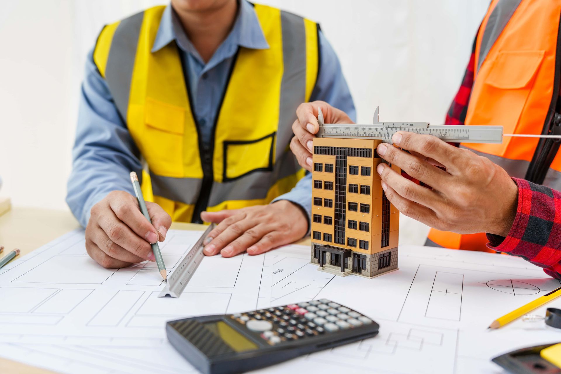 Two construction workers are sitting at a table looking at a model building.