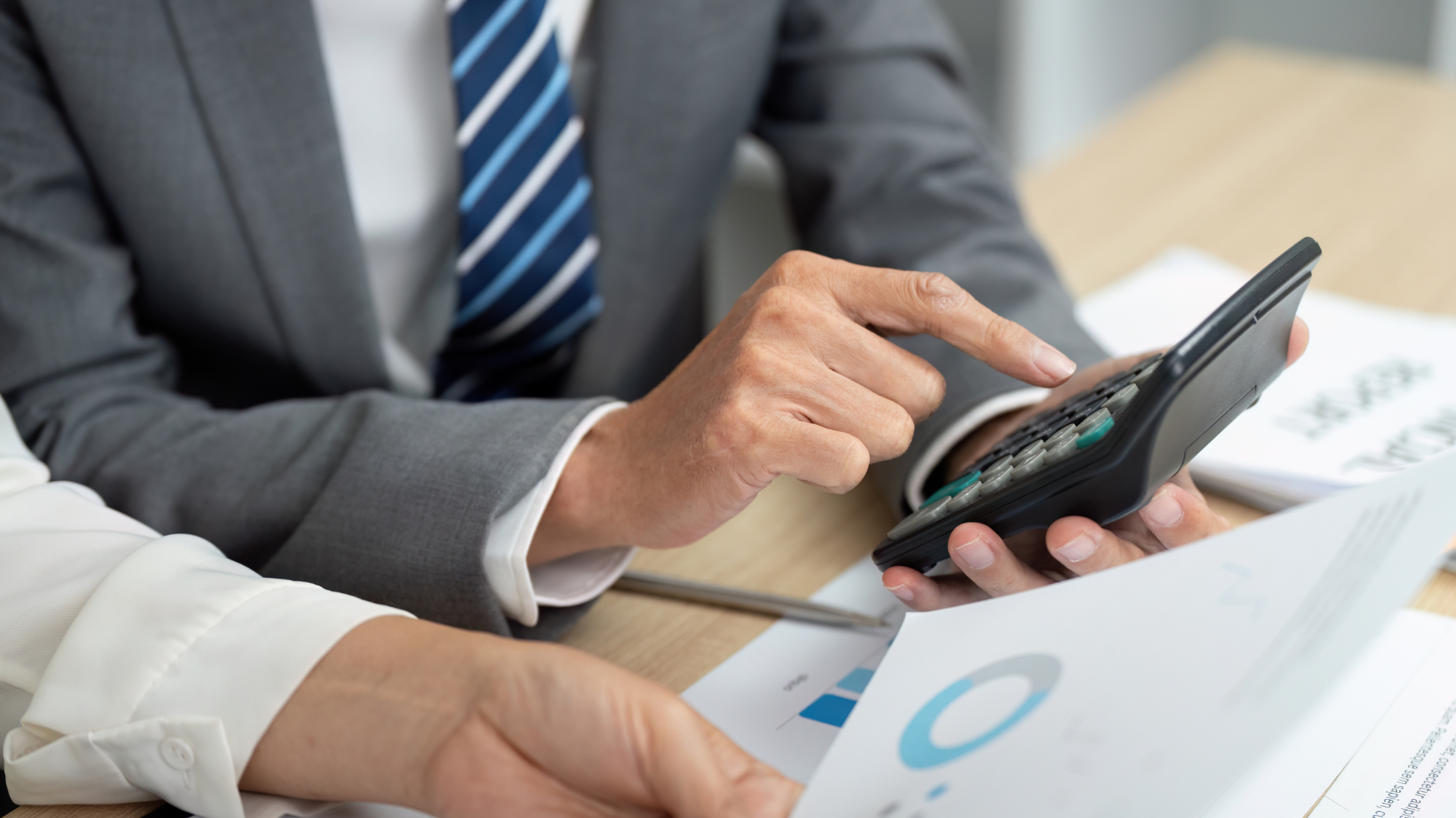 Business professionals reviewing financial charts and using a calculator at a desk.