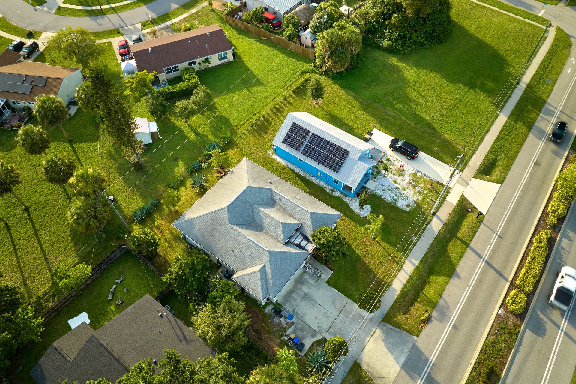 Aerial view of a suburban neighborhood with houses, lawns, and a road along the right side.