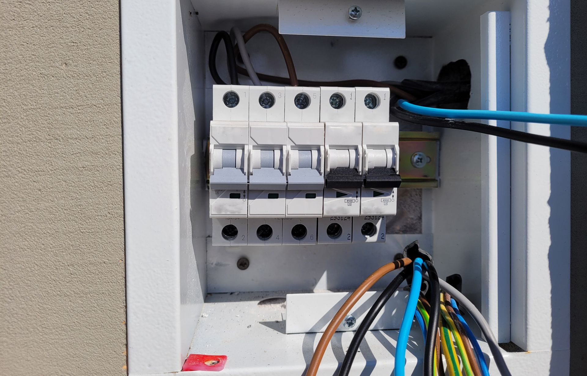 Open electrical breaker panel with multiple switches and exposed colored wires inside.