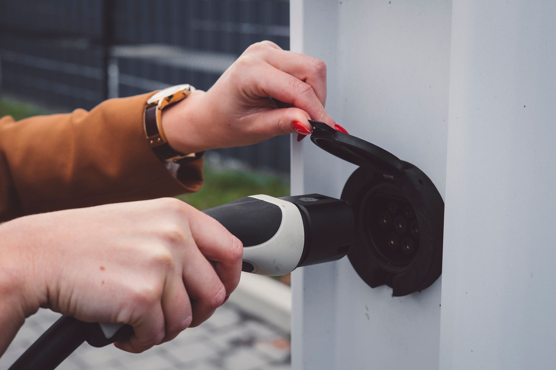 Hands plugging an electric vehicle charger into a white charging port
