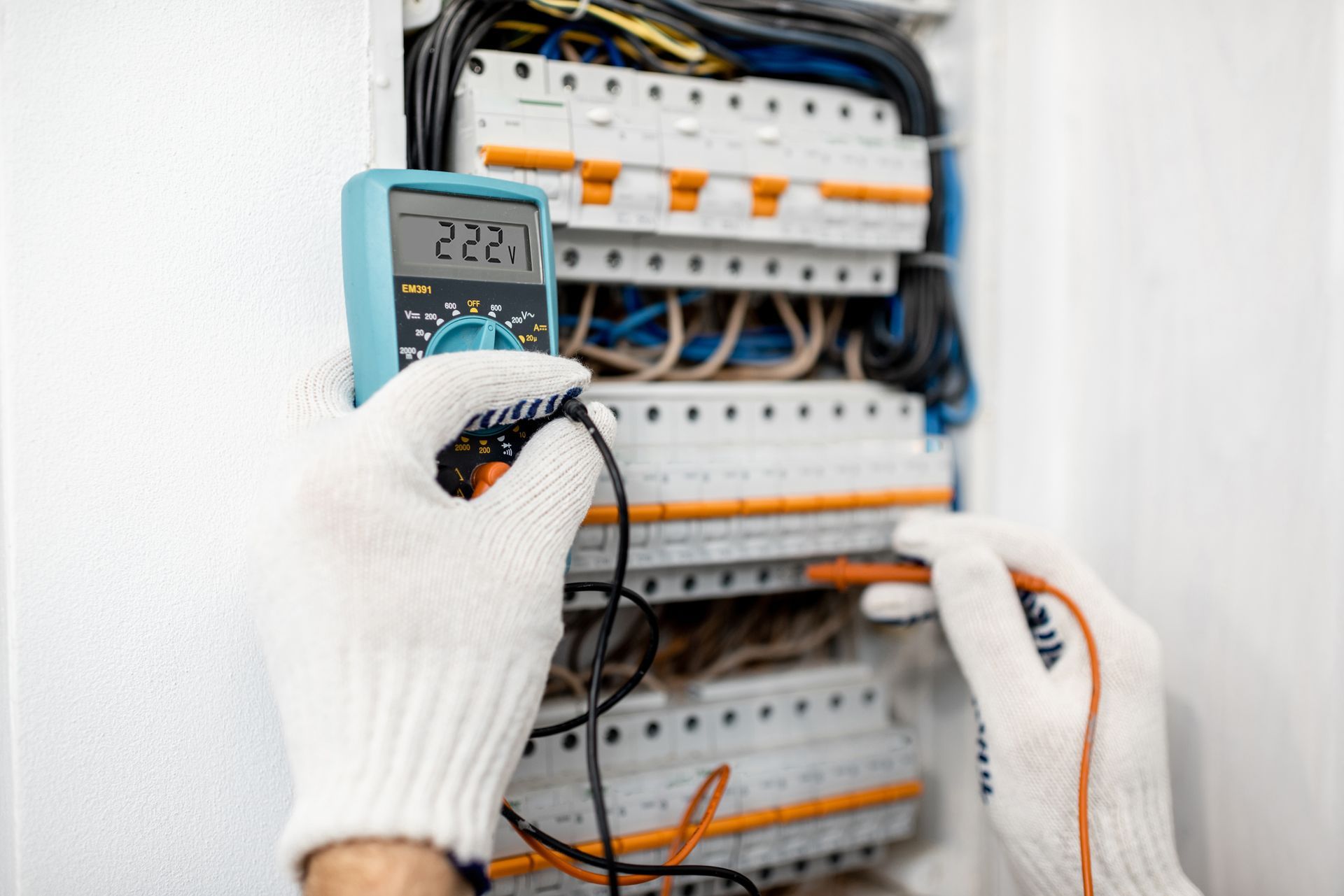 Hands testing an electrical breaker panel with a digital multimeter and wires.