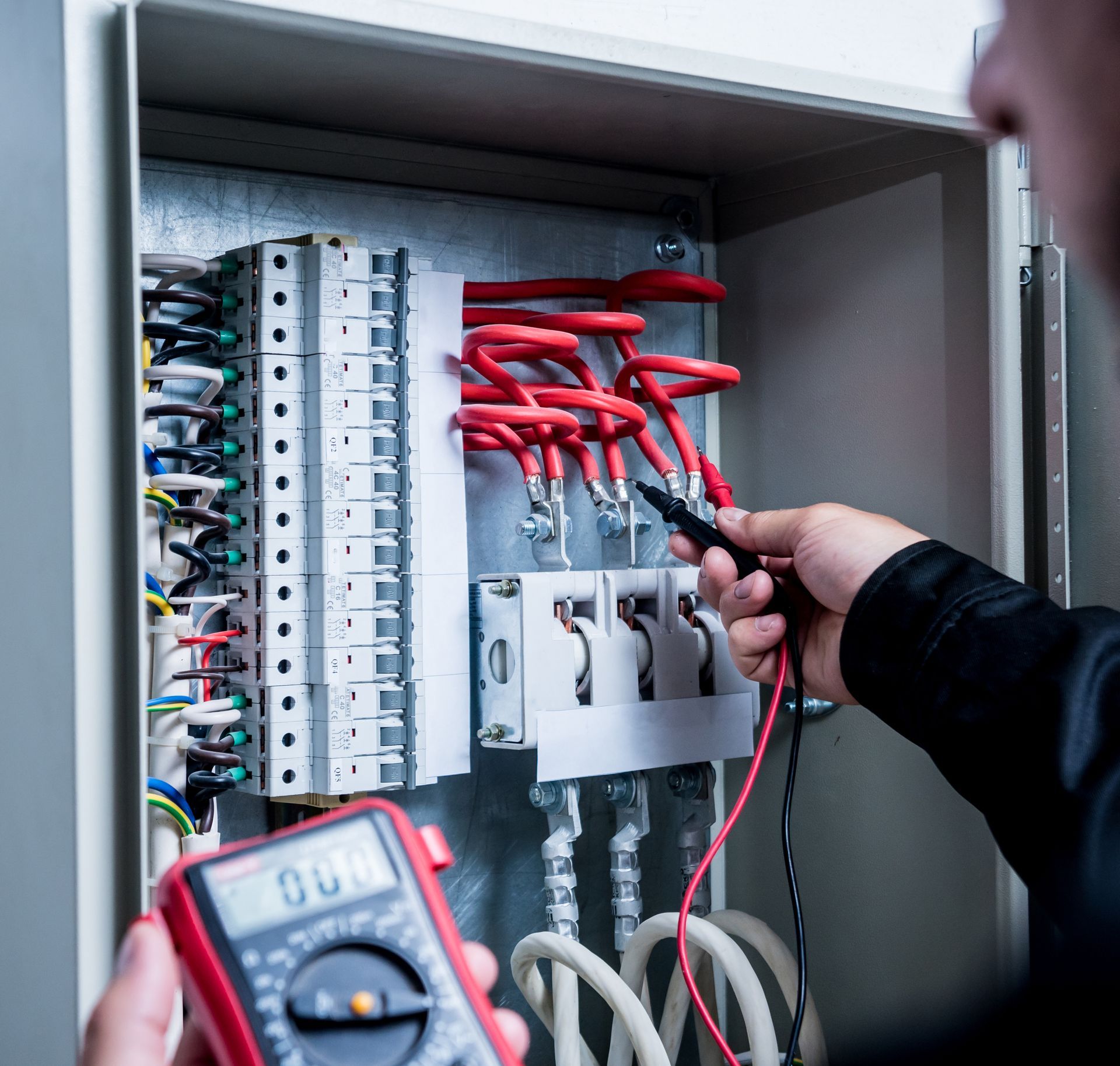 Electrician testing wires inside an open electrical panel with a multimeter.