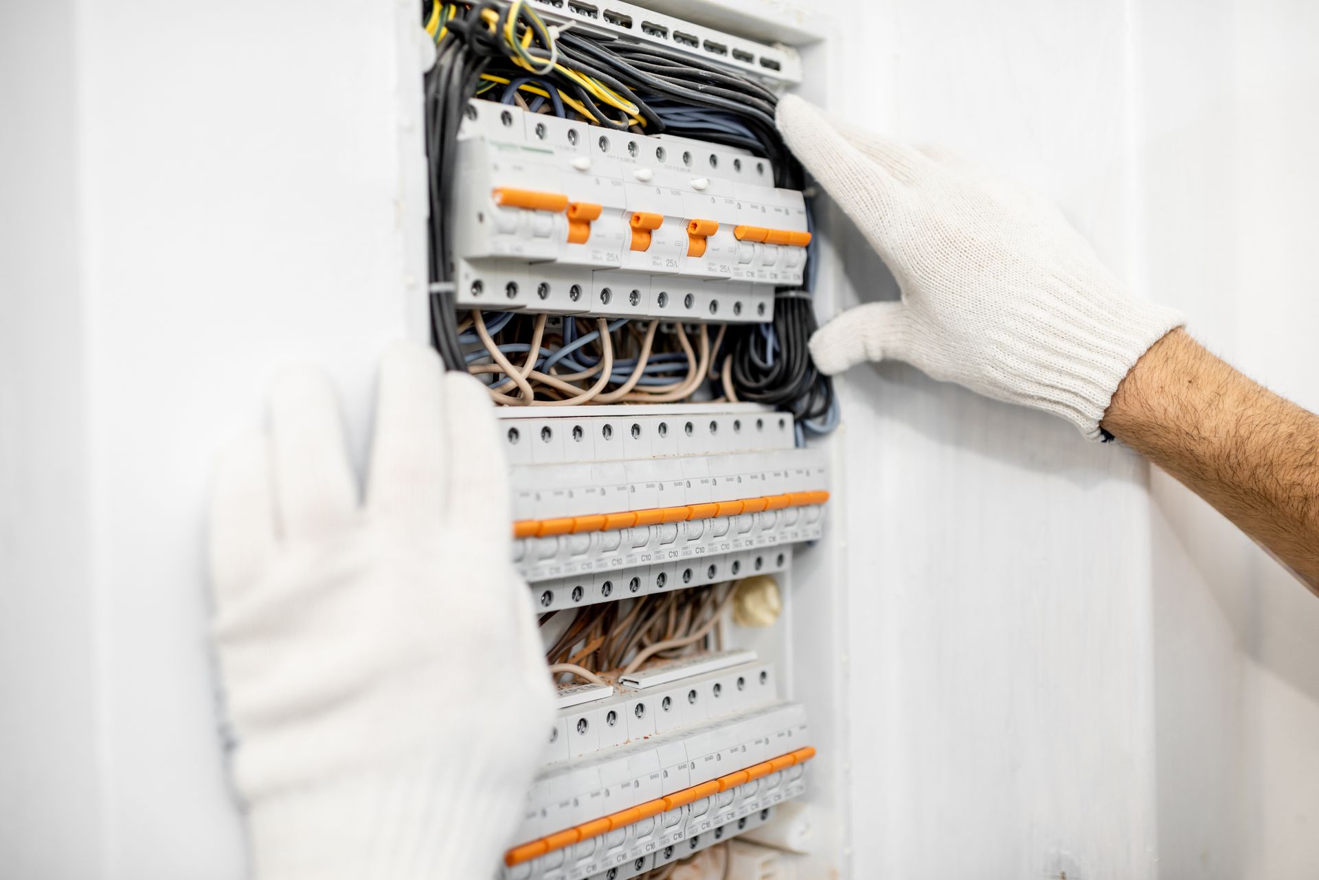 Gloved hands adjusting electrical circuit breakers in a white breaker panel
