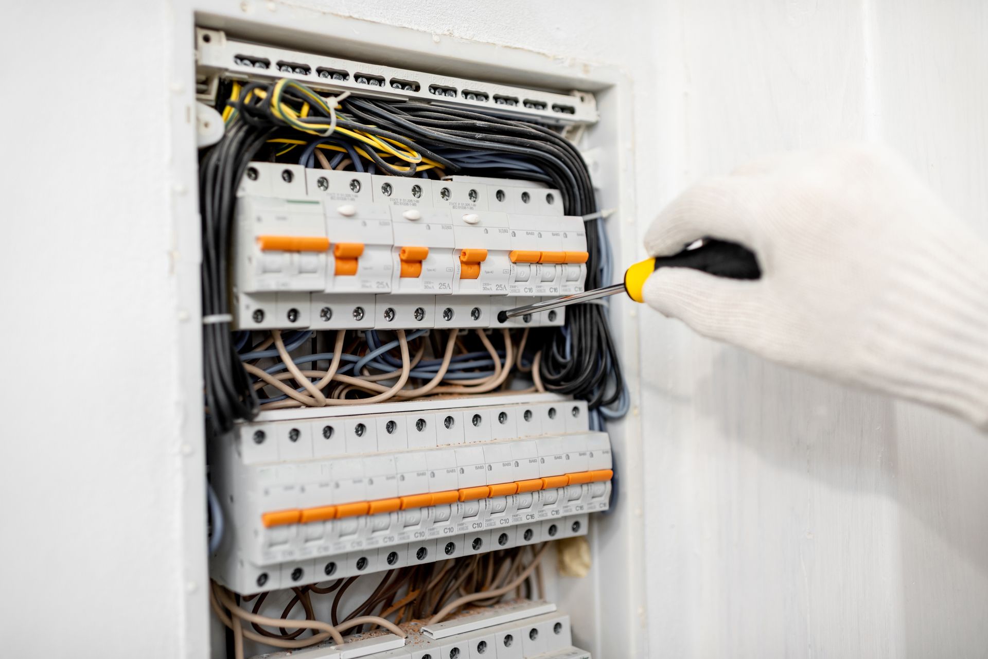 Electrical panel with circuit breakers being adjusted by a gloved hand using a yellow screwdriver