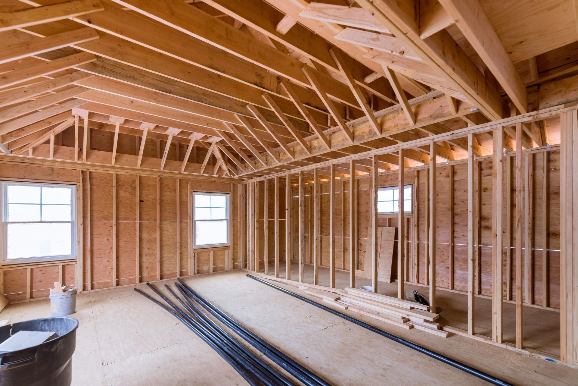 Interior view of a building under construction, showing wooden framing, windows, and exposed ceiling beams.