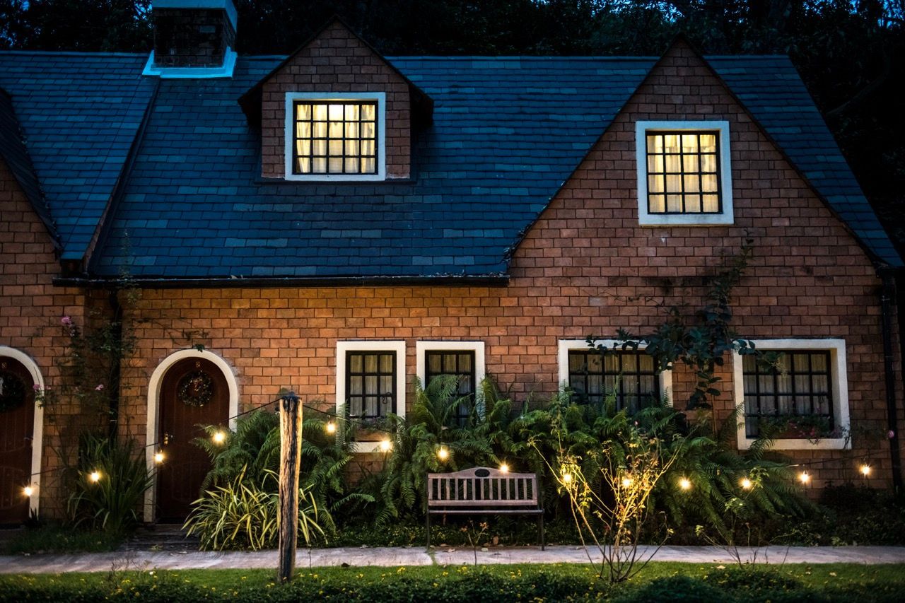 Brick house at night with lit windows, arched doorway, and illuminated front garden path