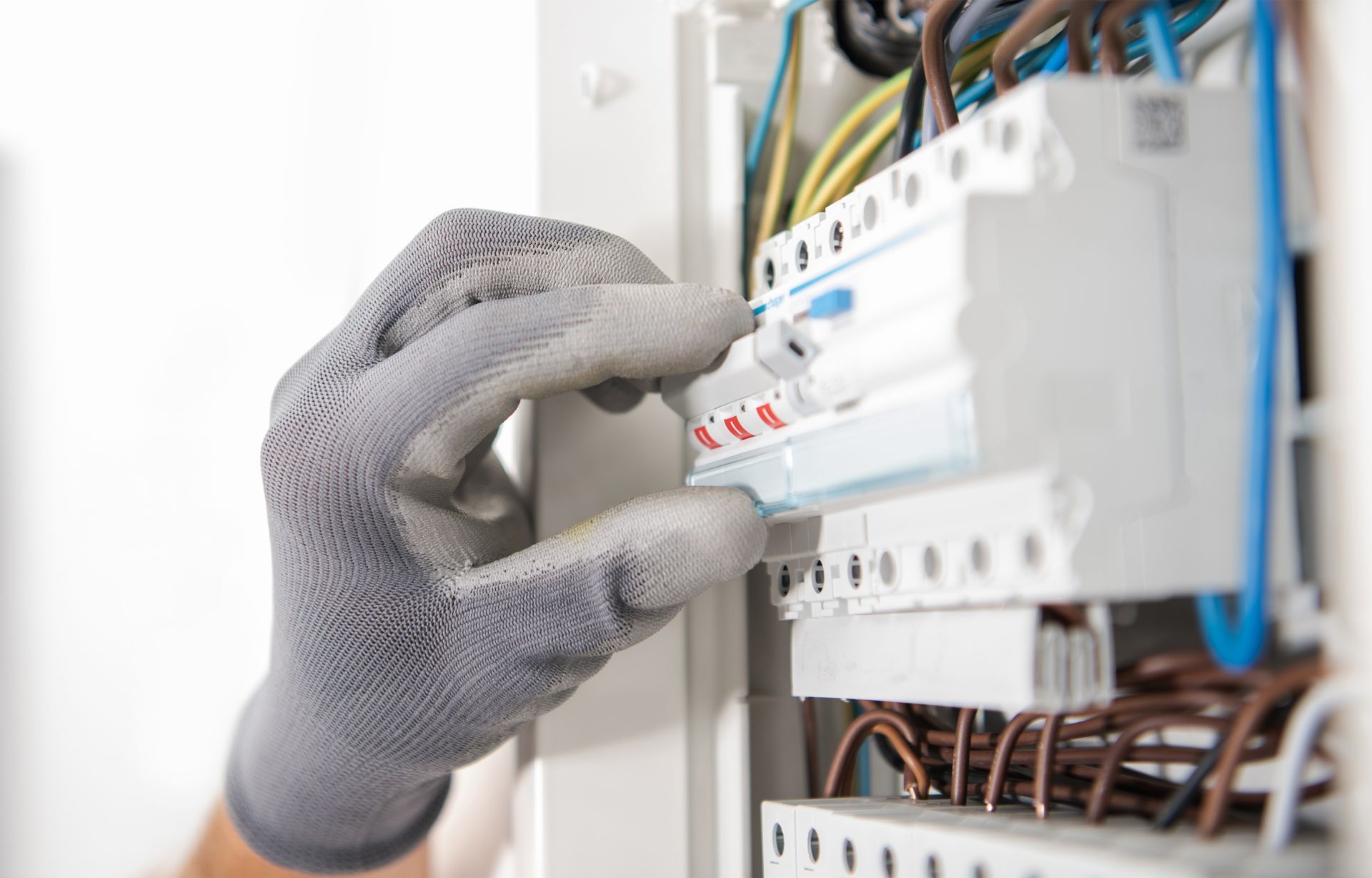 Gloved hand adjusting a circuit breaker in an electrical panel with exposed wires