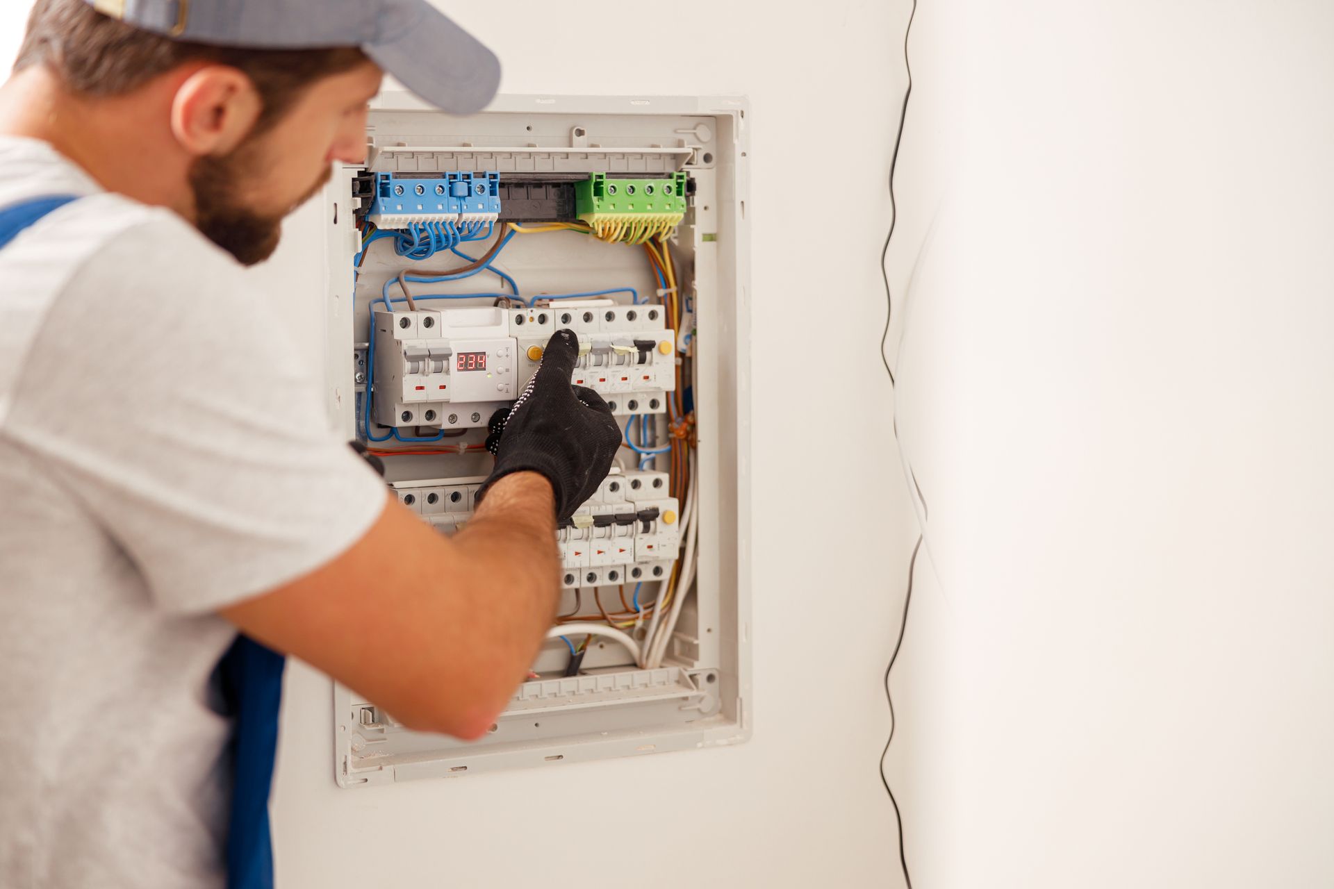 Technician inspecting electrical breaker panel inside a wall-mounted cabinet