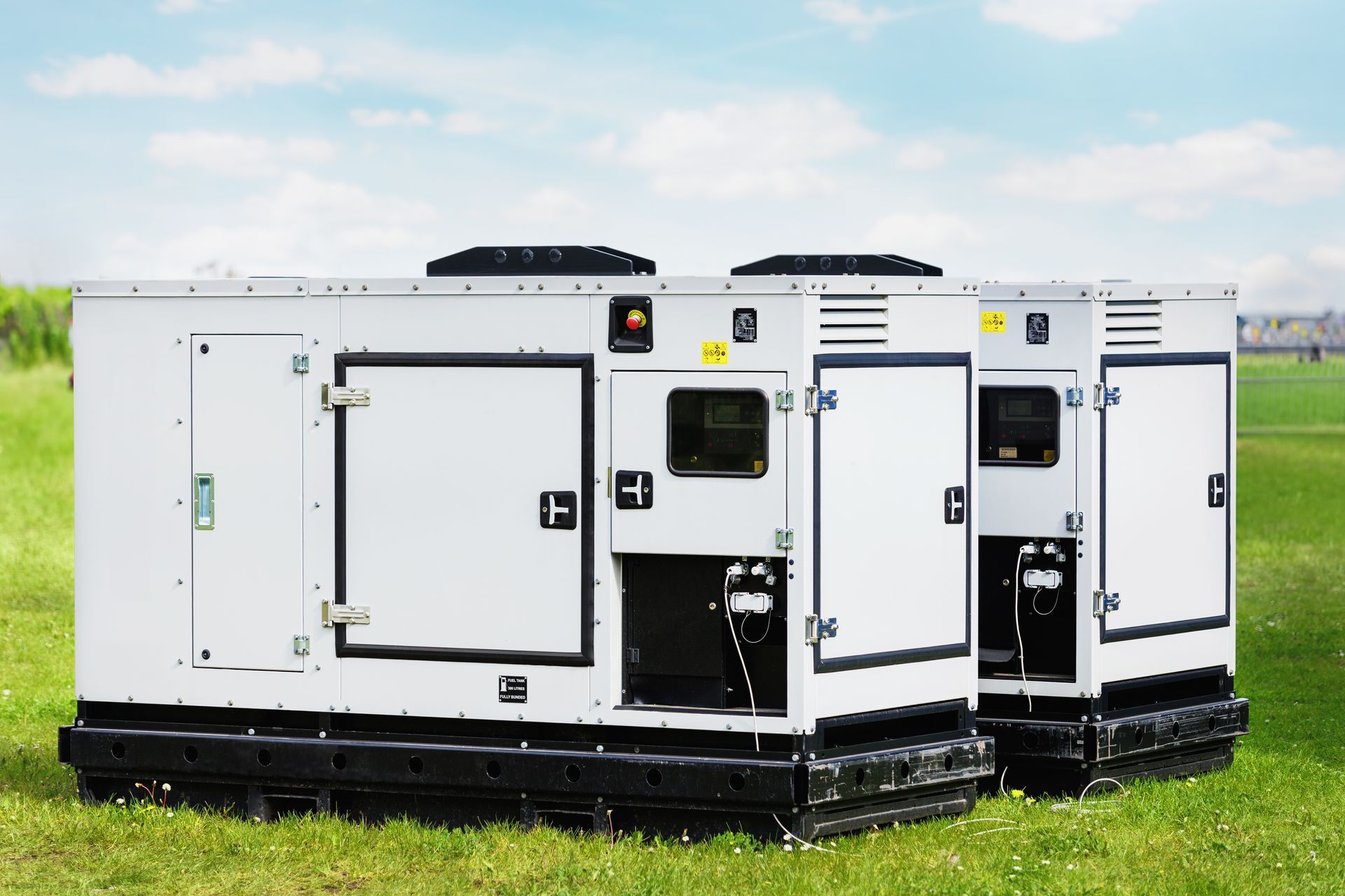White portable generators on black skids sitting in a grassy field