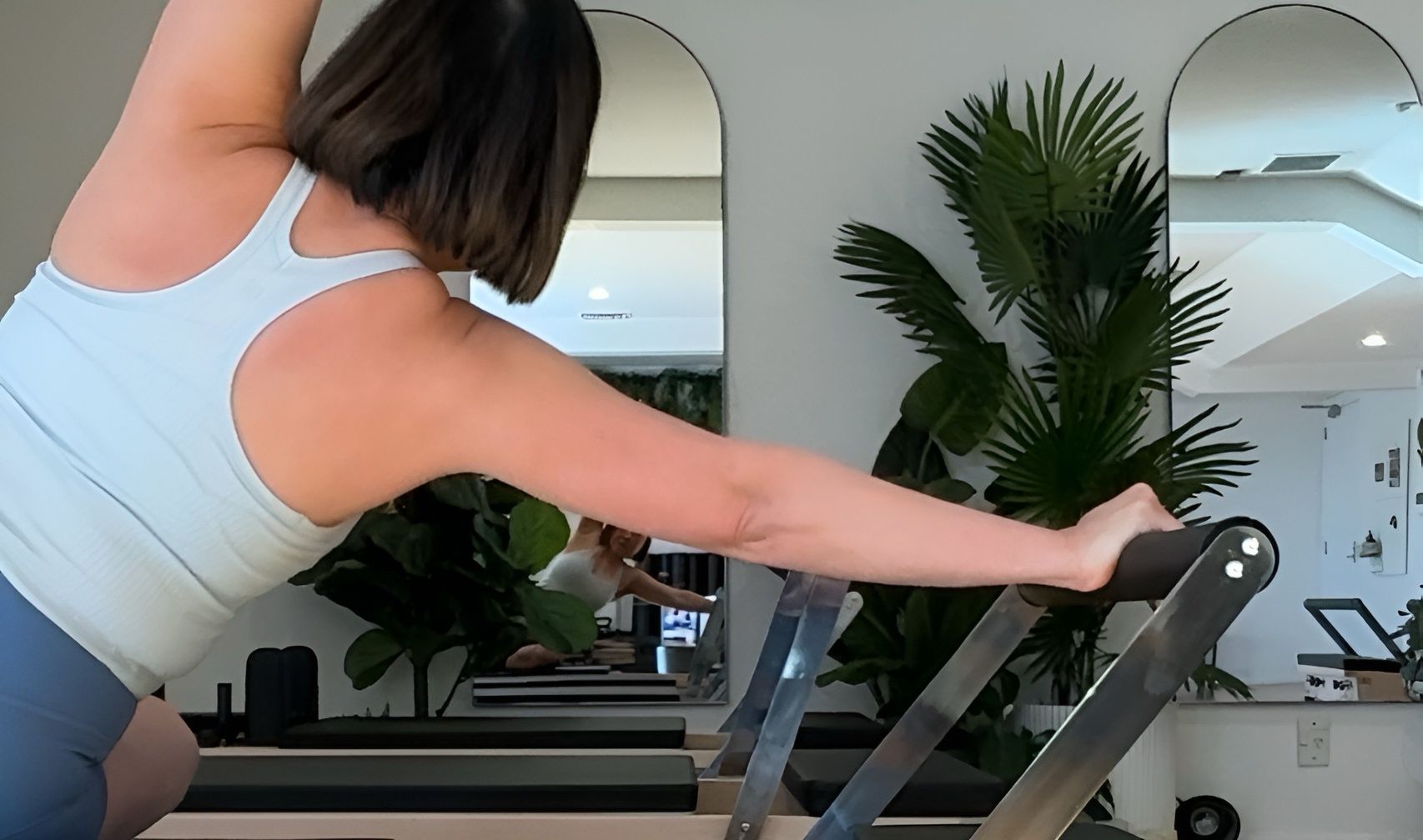 Person in black athletic wear holding a kettlebell, bending over in a white-walled gym.