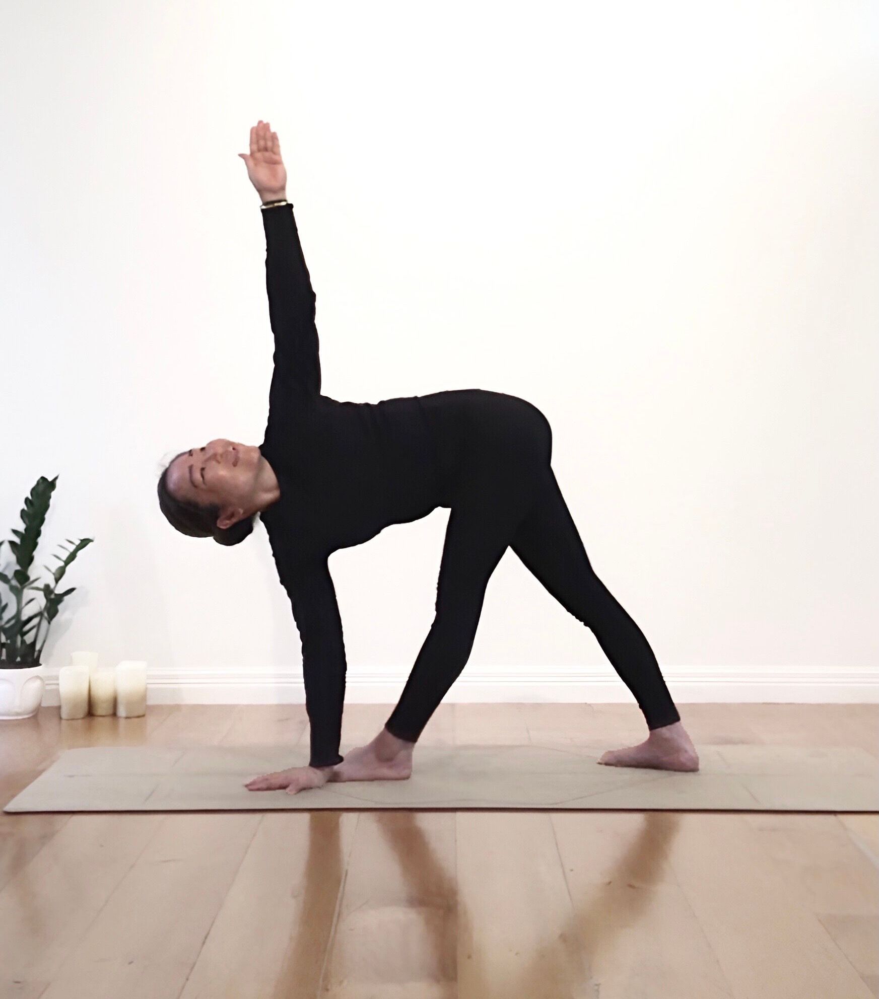 Woman in black yoga outfit in Triangle Pose on a mat, arm raised, indoors.