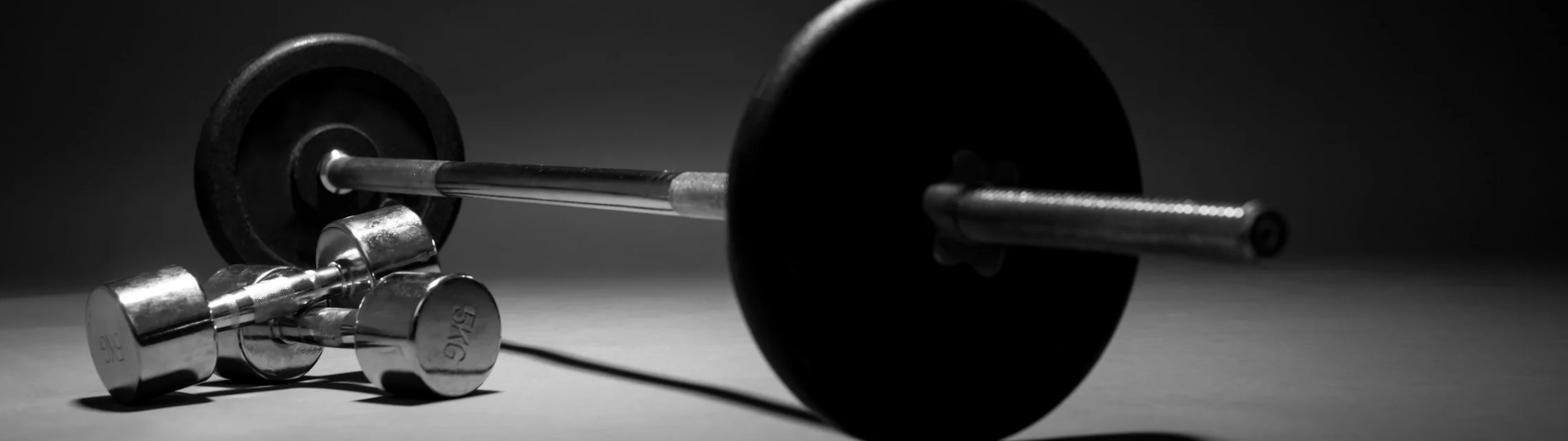 Barbell and dumbbells on a dark surface, suggesting a workout scene.