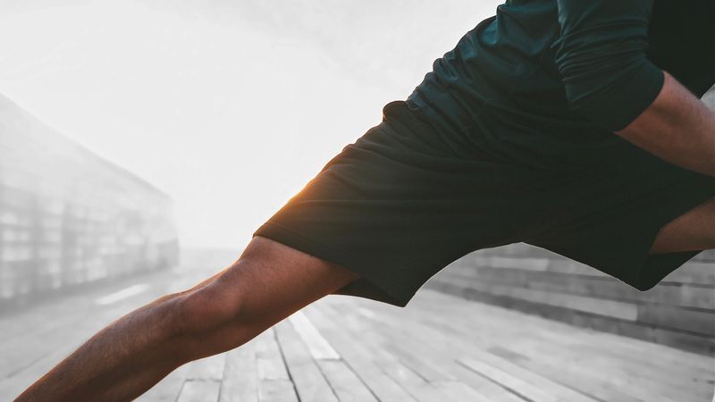 Person stretching leg outdoors in black athletic wear.