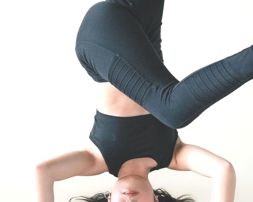 Woman upside down in yoga pose, wearing black activewear, against white background.