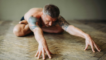 A person in a seated forward fold yoga pose, holding their feet with both hands on a gray mat.