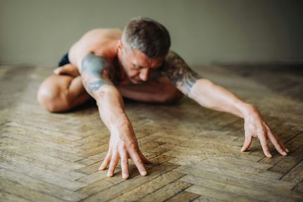 A person in a seated forward fold yoga pose, holding their feet with both hands on a gray mat.