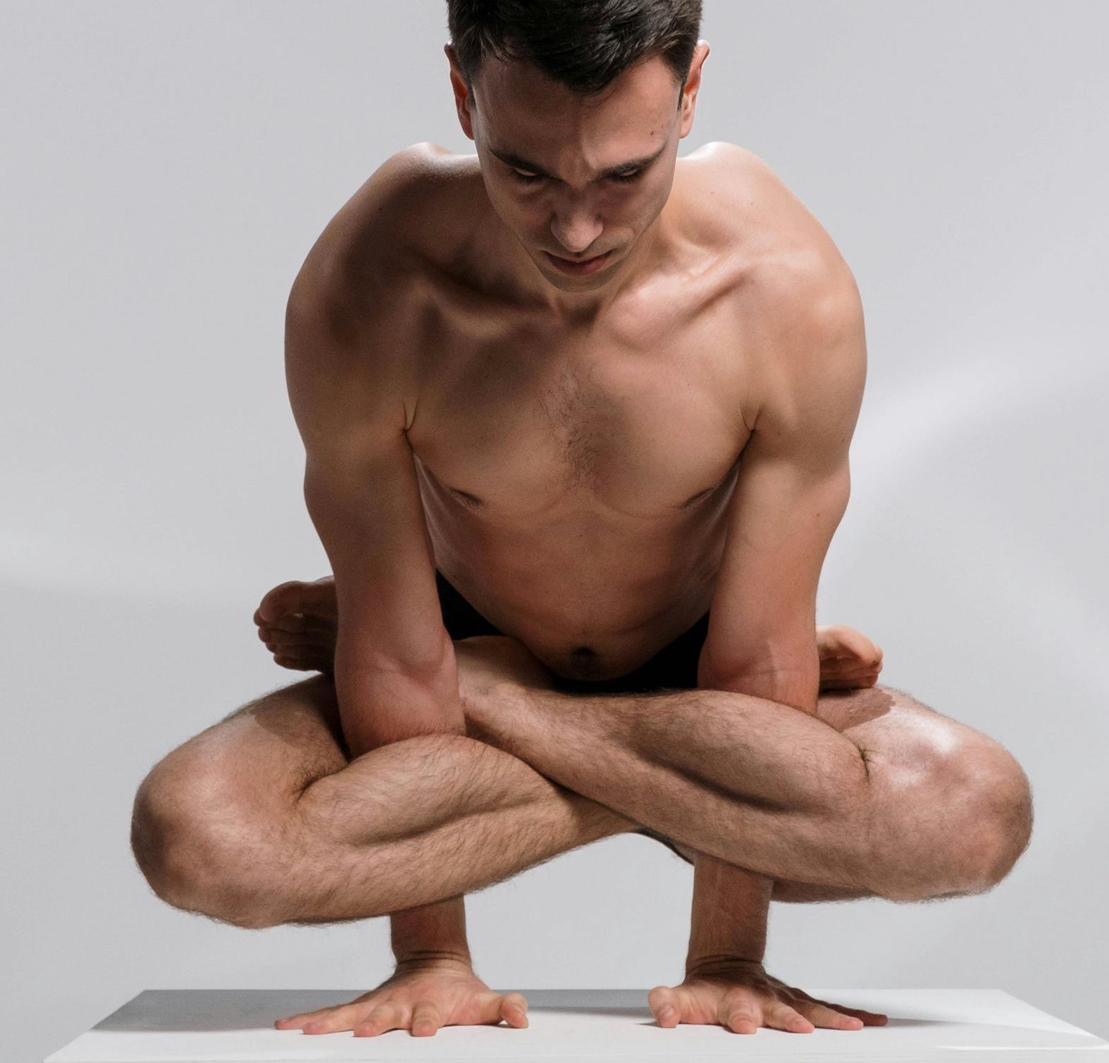 Man balances on hands in a yoga pose, legs crossed, looking down.