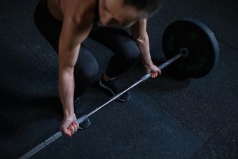 A person in a gym preparing to lift a barbell from the floor, hands gripping the textured metal bar.