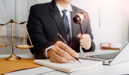 A judge is sitting at a desk holding a gavel and writing in a notebook.